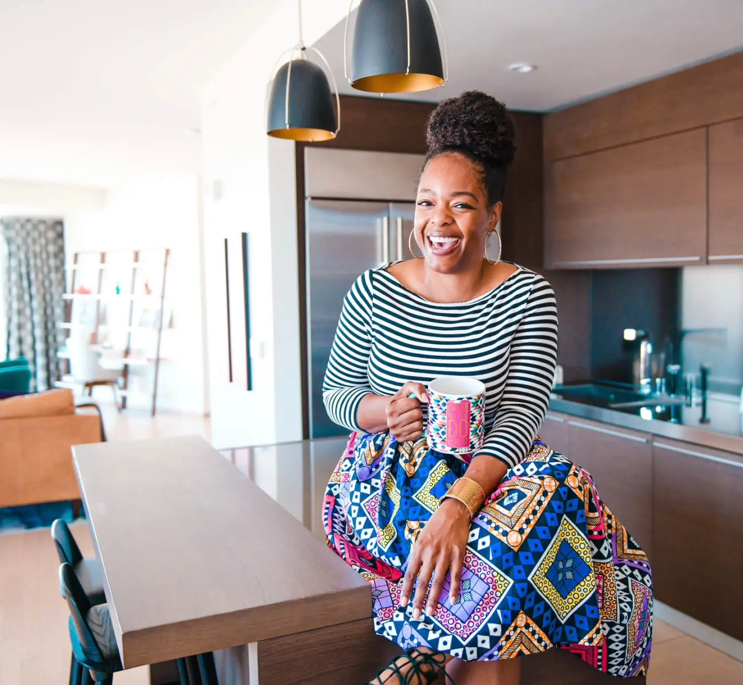Entrepreneur Apryl Thatch, smiling and colourfully dressed, sitting on a kitchen table