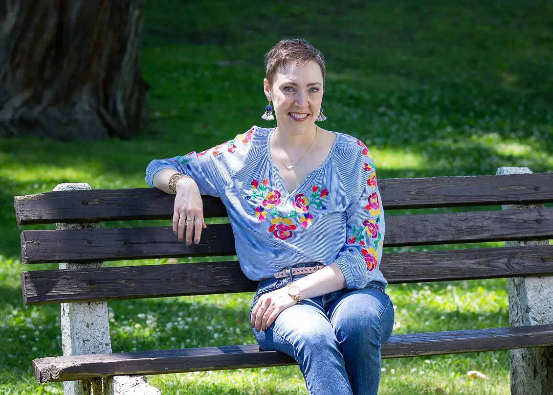 Life coach Penny Casselman sitting on a wooden bench in a lush green park.