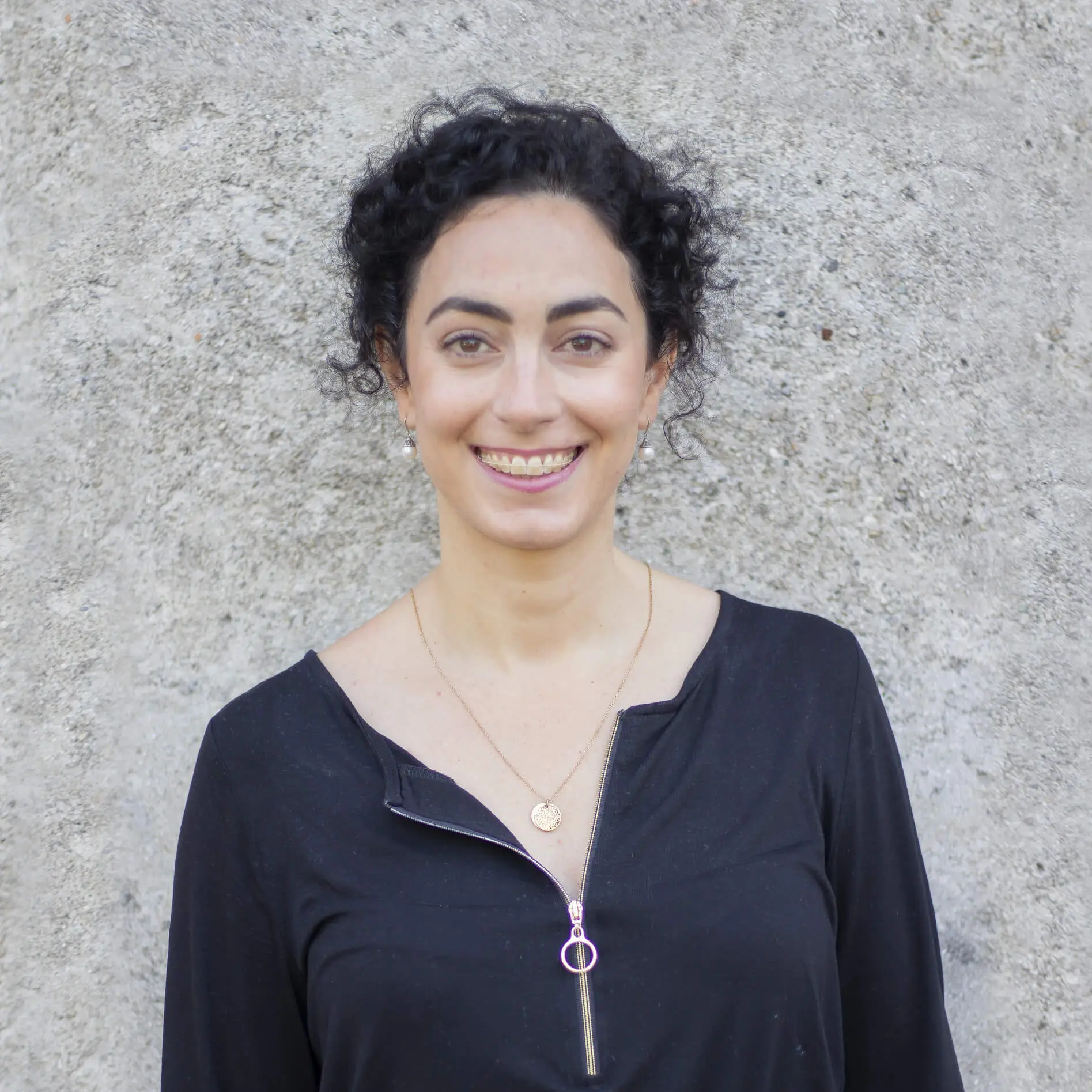Mindfulness Teacher Roya Hekmatpanah smiling and standing in front of a concrete wall
